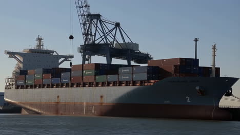 a large container ship docked at a port with a gantry crane operating nearby
