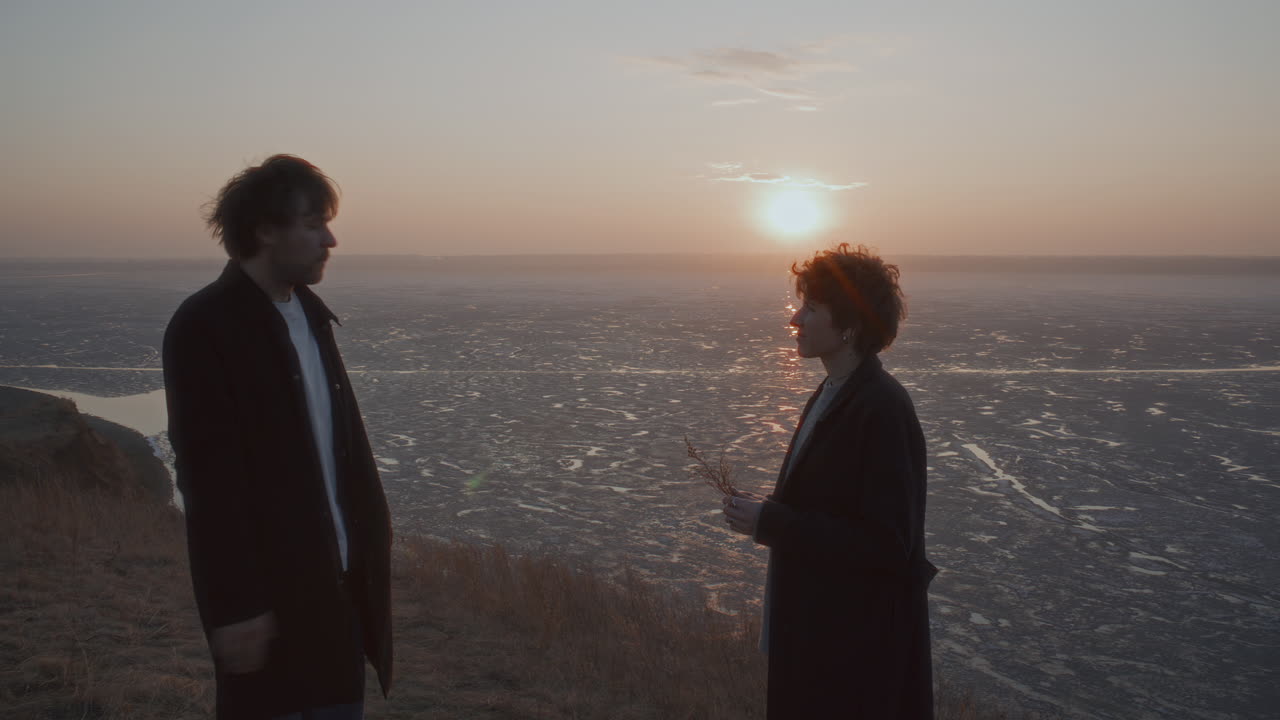 Couple Smoking and Speaking on Shore of Frozen Lake at Sunset