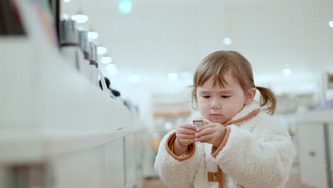 Curiosa-Niña-De-3-Años-Recogiendo-Un-Elemento-De-Barra-De-Oro-Que-Se-Muestra-Dentro-De-Un-Centro-Comercial