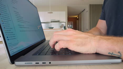 hombre escribiendo rápidamente en su computadora portátil en la encimera de la cocina