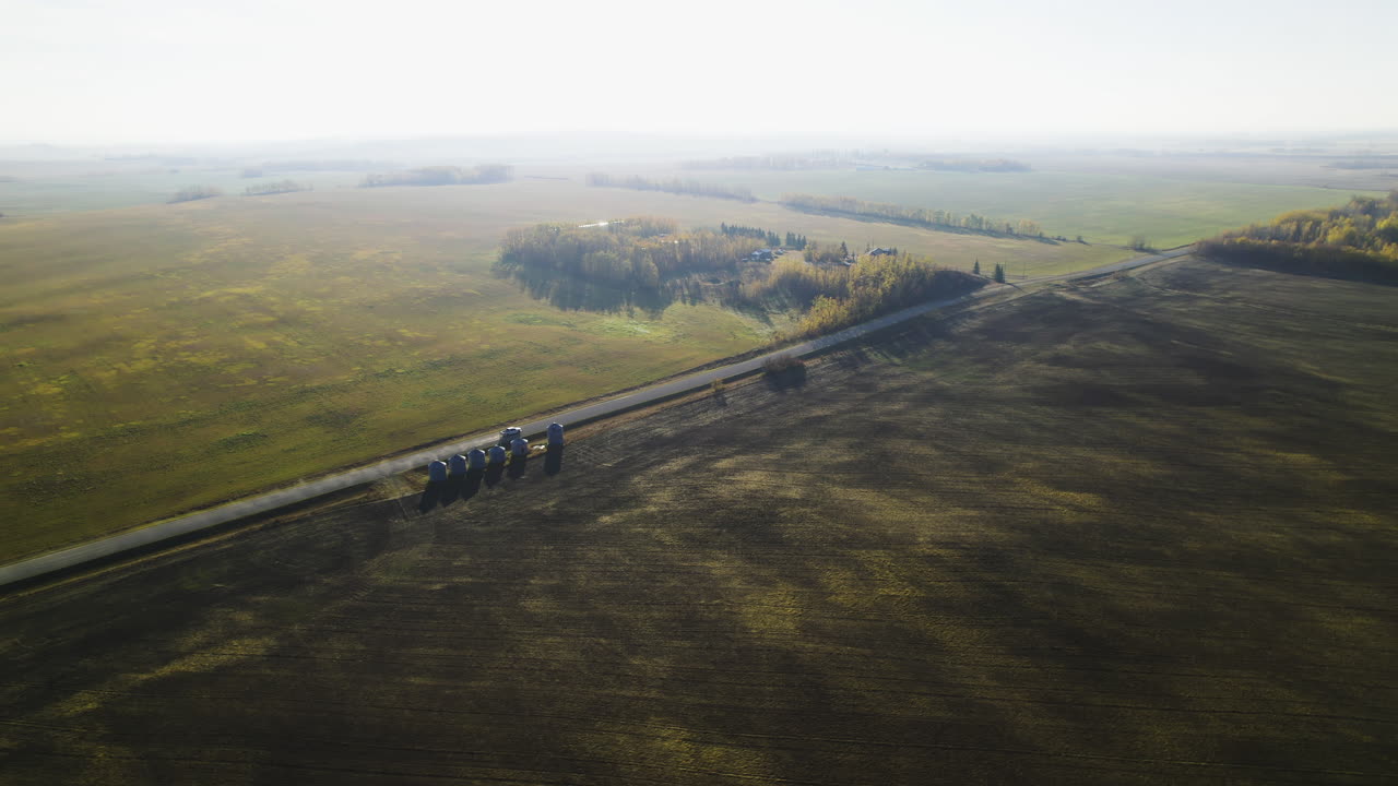 Aerial View Of Pickup Truck Driving Through Wheat Crops Field With Silos On The Road.