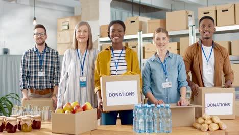 grupo multiétnico de voluntarios empacando cajas con comida y ropa en un almacén de caridad y sonriendo a la cámara