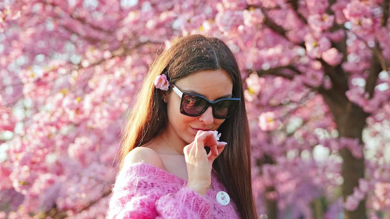 Closeup beauty moment of woman gently smelling pink petal in soft spring sunset