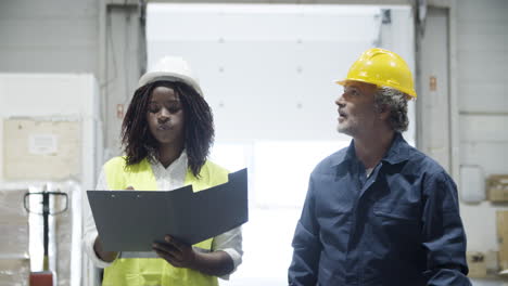 trabajadores multiétnicos en casco caminando y contando bienes en stock