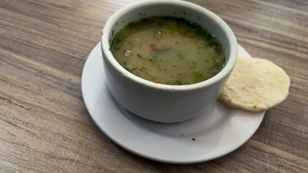 Panoramica lenta di una zuppa di erbe chiara servita con una piccola arepa colombiana