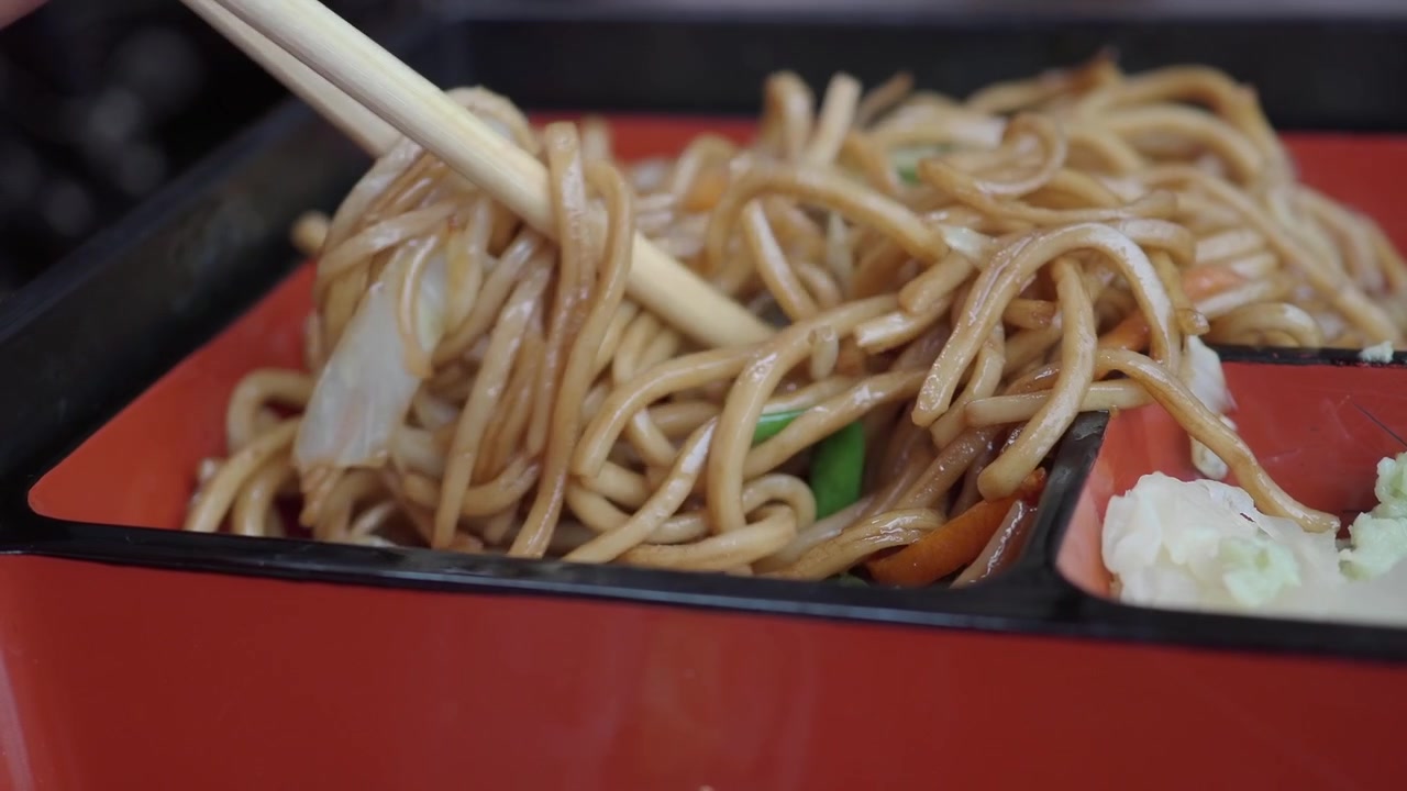 Persona che mangia noodles saltati con le bacchette da una bento box