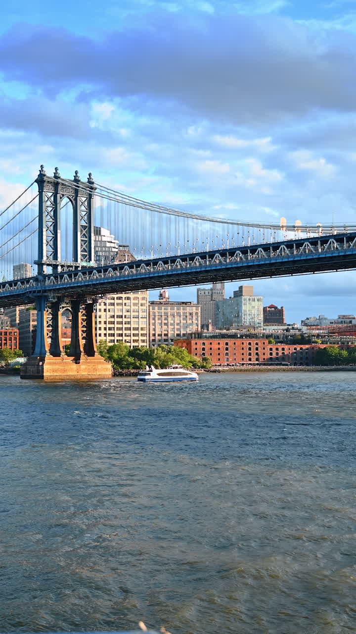 Water transport moves by the waterscape of the East River. Low angle view on the support of the Manhattan Bridge. Vertical video