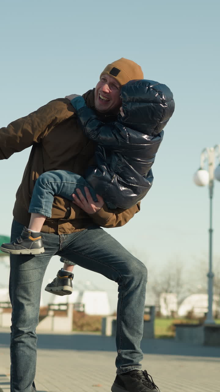 vicino al padre che porta suo figlio mentre tiene la ringhiera con la mano destra e appende una gamba in aria, entrambi ridono e sono felici mentre gioca e pende