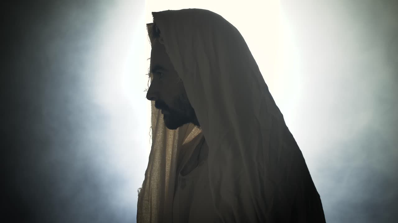 Jesus Christ resurrected on Easter Sunday inside empty tomb in bright, shining light, wearing white hood and robe. Cinematic Christian resurrection visual.