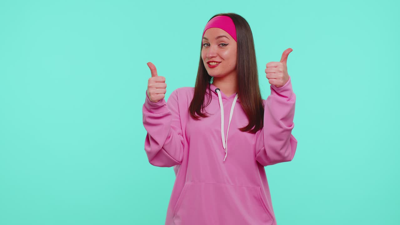Teen stylish girl in pink hoodie showing thumbs up and nodding in approval successful good work