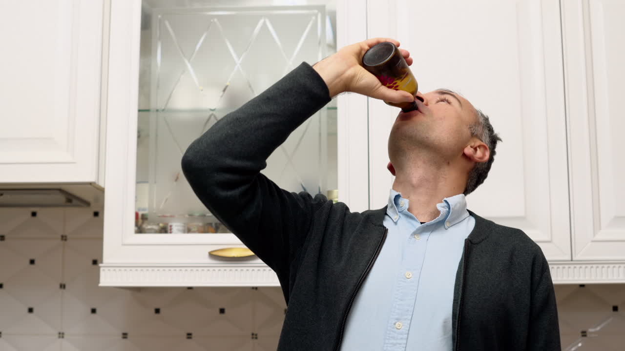 Man drinking kombucha from a brown glass bottle in the kitchen