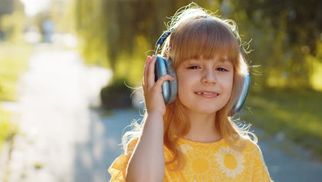 Happy-child-girl-in-wireless-headphones-choosing,-listening-music-in-smartphone-dancing-outdoors