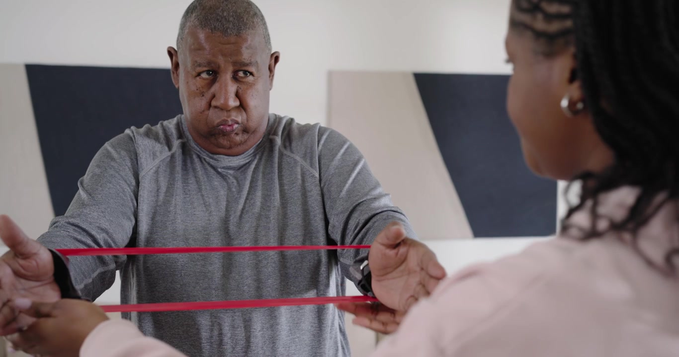 Father pressing and breathing for rehab, daughter looping and guiding red band in living room