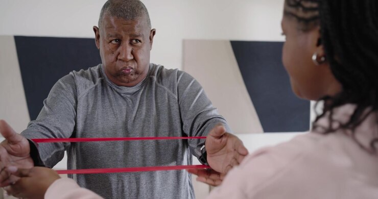 Father pressing and breathing for rehab, daughter looping and guiding red band in living room