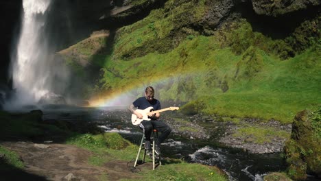 Hombre-Tocando-La-Guitarra-Frente-A-Una-Hermosa-Cascada-En-Islandia