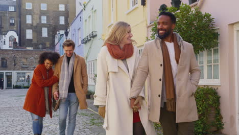 grupo multicultural de amigos abrazados mientras caminan por la calle empedrada de mews en visita a la ciudad en otoño o invierno - filmado en cámara lenta