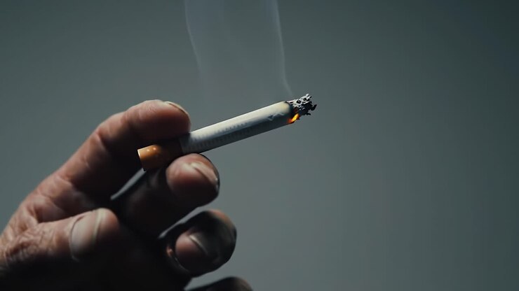 Close-up of Hand Holding Burning Cigarette Against Gray Backdrop in Dim Light Ambiance