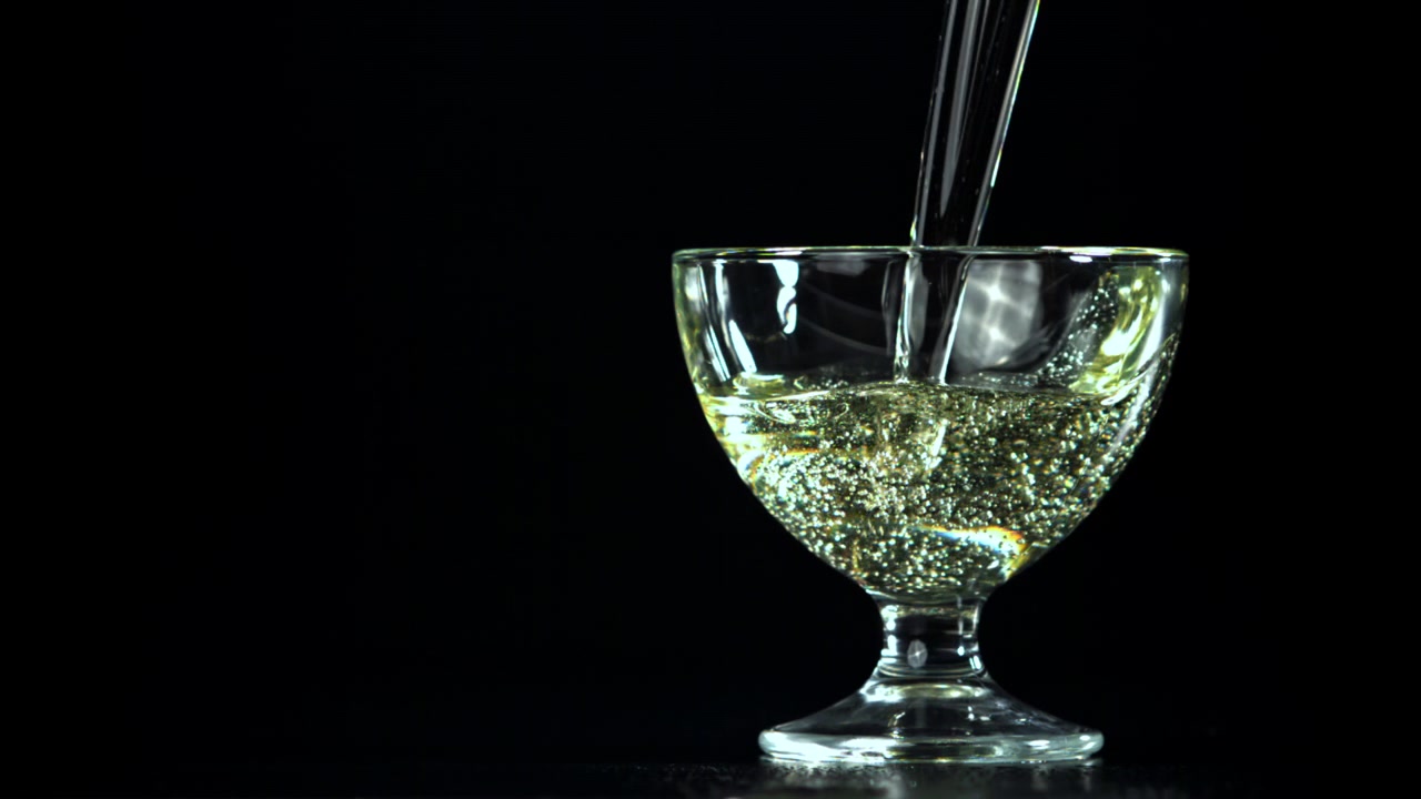Liquido trasparente versato in un calice di vetro su sfondo nero