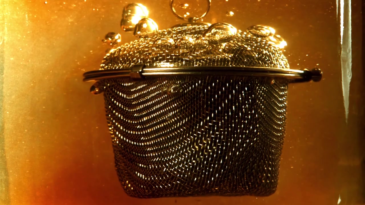Infuseur à thé métallique submergé dans un liquide doré chaud, créant des bulles