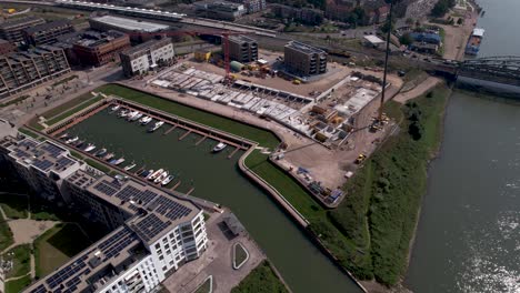 backwards aerial movement showing construction site of luxury apartment building at river ijssel riverbed revealing the wider urban cityscape with skyline of tower town zutphen in the background
