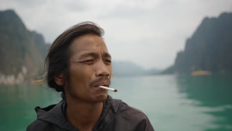 man smoking on a boat in a scenic lake with mountains