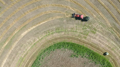 Toma-De-Arriba-Hacia-Abajo-De-Un-Tractor-Empacando-Heno-En-Las-Tierras-De-Cultivo-En-Saskatchewan,-Canadá-En-Un-Día-Soleado---Drone-Aéreo