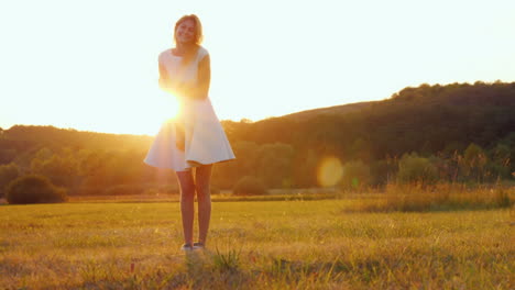 beautiful young woman in a light summer dress standing in a meadow in the rays of the setting sun lo