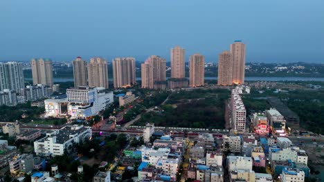 aerial view captures an urban skyline at dusk with numerous high-rise residential and commercial buildings. a busy illuminated street with traffic runs through the foreground