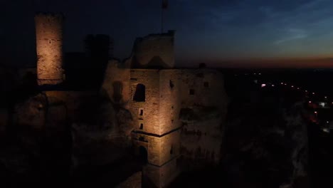 Ethereal-drone-footage-captures-the-majestic-Ogrodzieniec-castle-illuminated-against-the-night-sky,-weaving-a-tale-of-mystery-and-grandeur