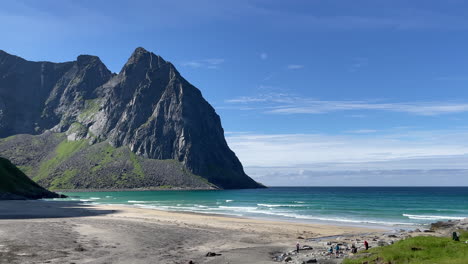 high mountain next to a turquoise water beach with waves on a sunny summer day