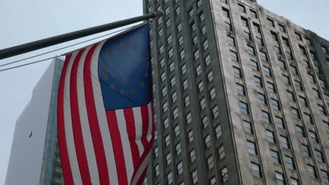 american flag blows proudly in the wind with large building behind it