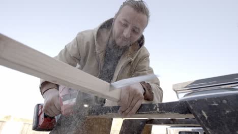 young caucasian man cutting wood with reciprocating saw, slow motion low angle