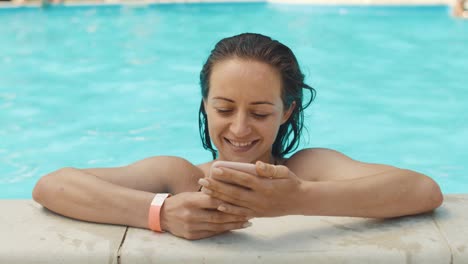 una mujer joven usa un teléfono inteligente en una piscina.