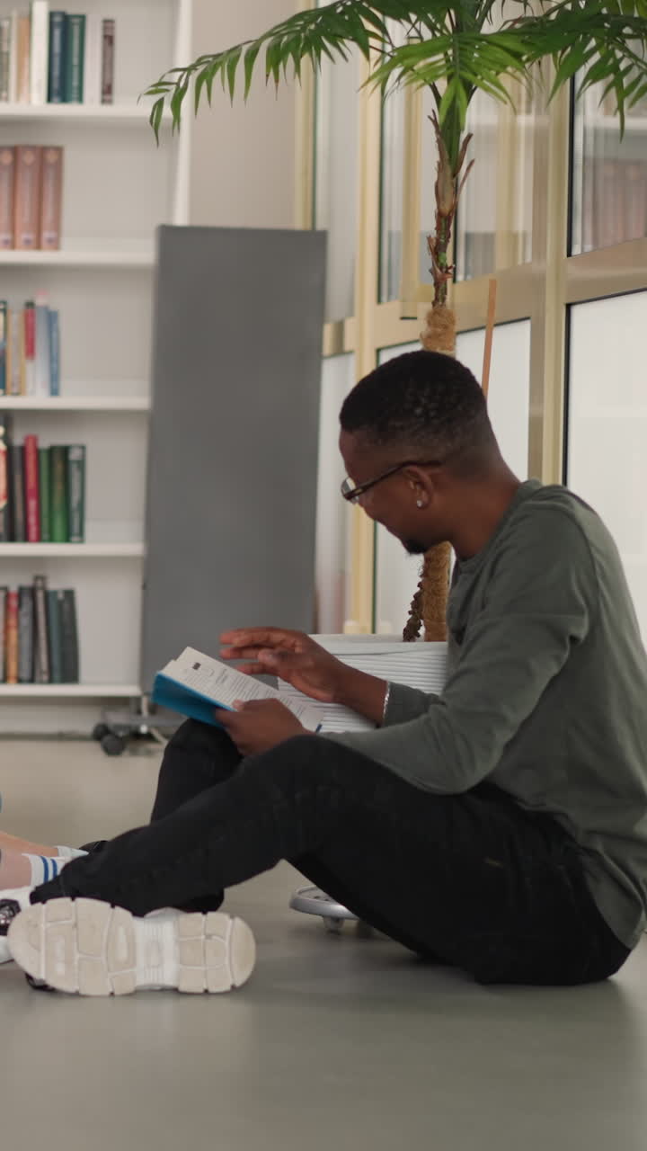 estudiantes felices disfrutan de la lectura de libros humorísticos en la biblioteca. hombre negro coquetea con mujeres bonitas durante la reunión del club de lectores en la librería. ocio intelectual