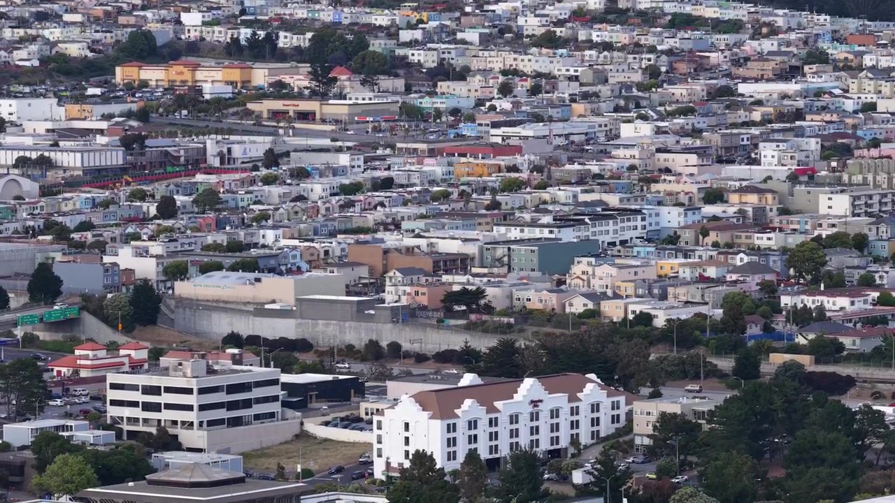 Vasta espansione urbana di un quartiere densamente popolato a Daly City, California, con case ed edifici fittamente raggruppati che coprono le dolci colline sotto un cielo nuvoloso