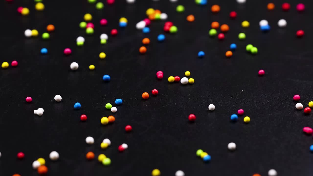 A close-up view of colorful sprinkles scattered randomly across a dark background, creating a lively pattern.