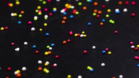 a close-up view of colorful sprinkles scattered randomly across a dark background, creating a lively pattern.