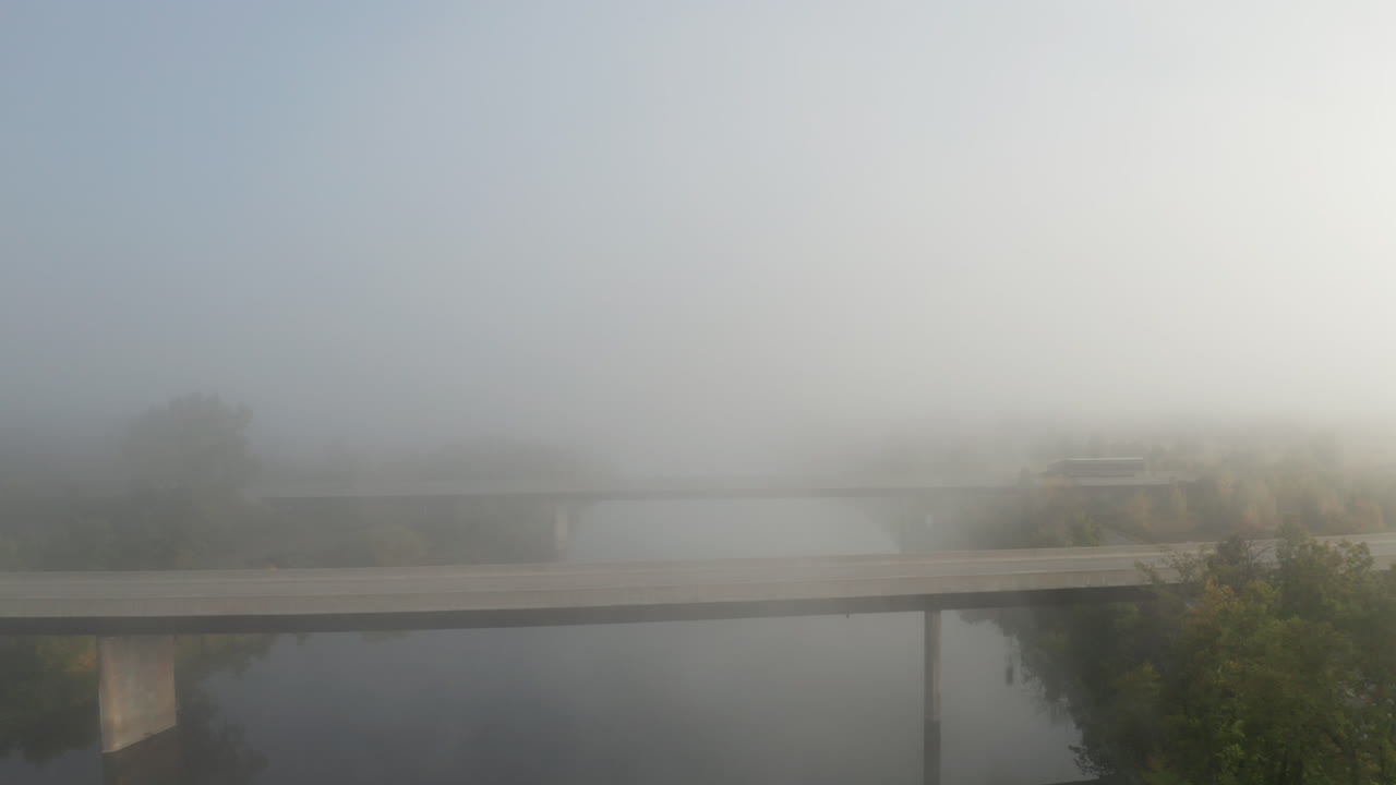 평화로운 강을 건너는 고속도로 교량에서 멀어지는 무인 항공기가 풍경 위에 걸려있는 안개 속으로 올라갑니다.