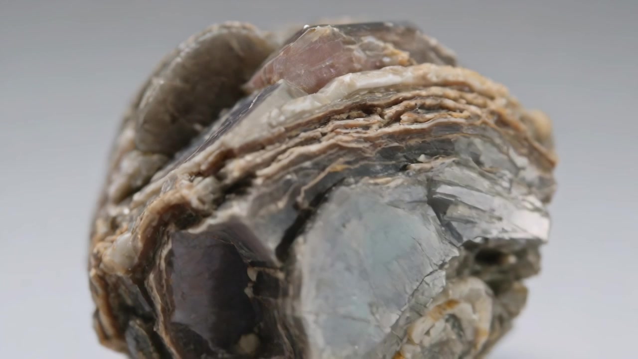 Telecamera che si allontana rivelando un campione minerale stratificato su superficie grigia, luce soffusa che rivela gli strati