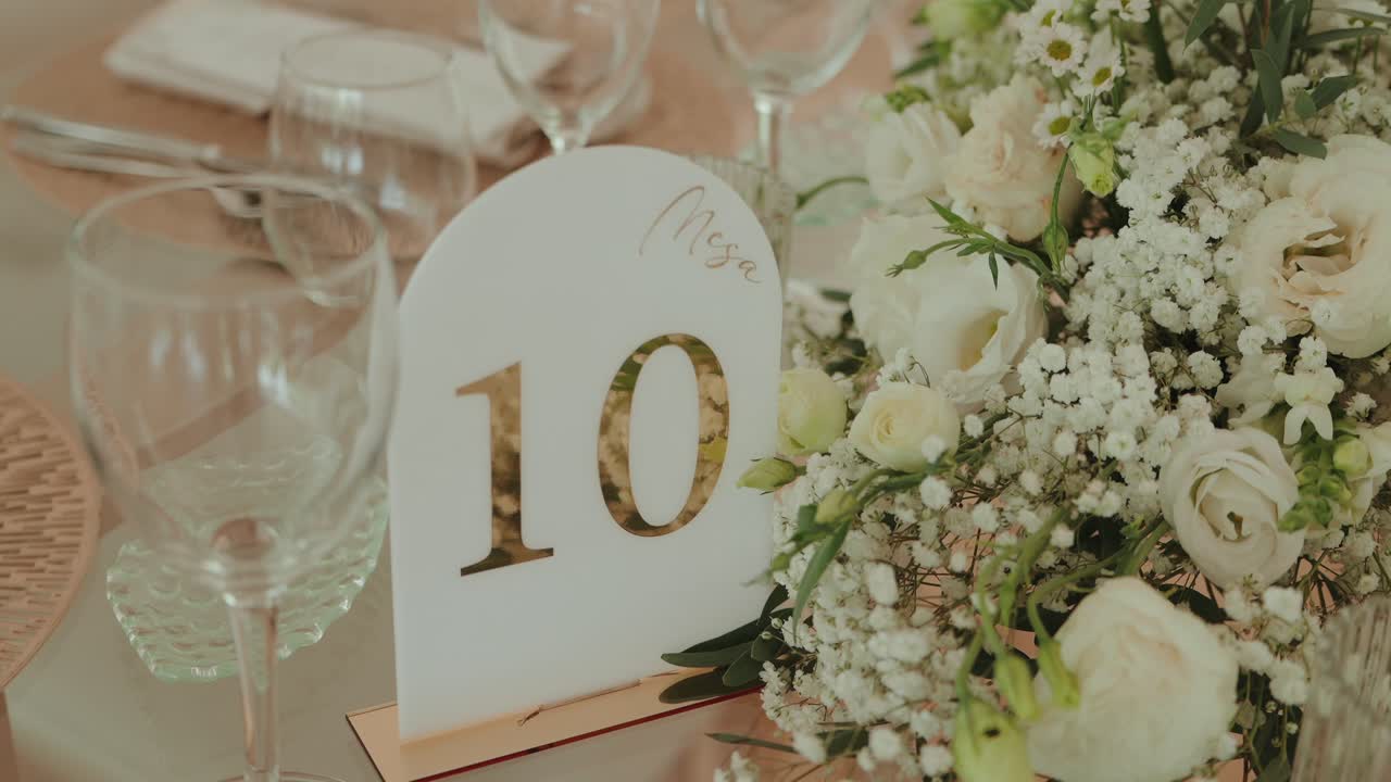 Número de mesa elegante para boda con flores y disposición de cristalería