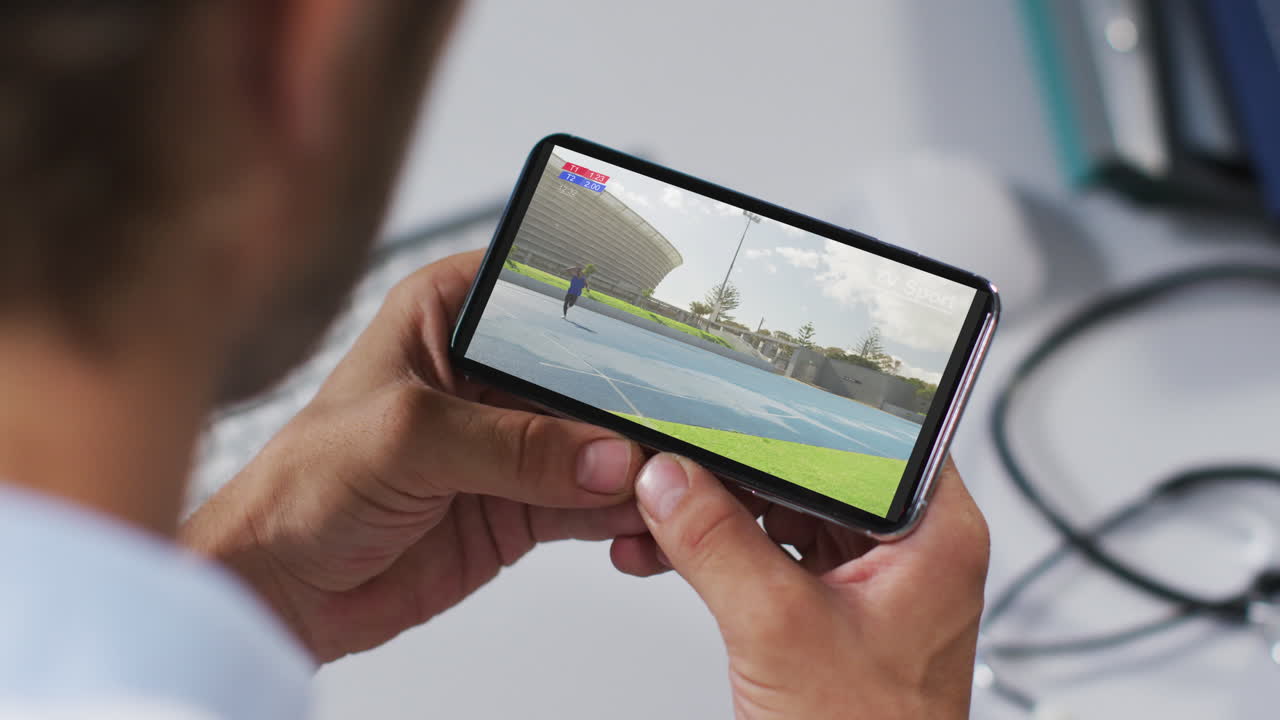 compuesto de un médico masculino viendo un evento de jabalina de atletismo en un teléfono inteligente