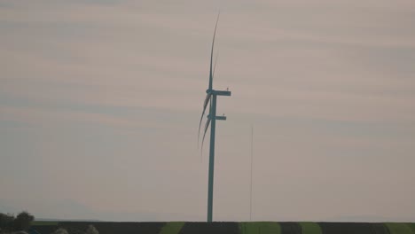 Slow-motion-shot-of-a-wind-turbine-in-a-field-during-sunset