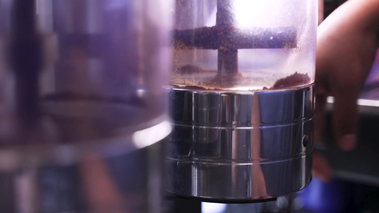 Customer hand pulls the handle on a bulk grinder dispenser as ground beans fall into a bag at a food store coffee station.