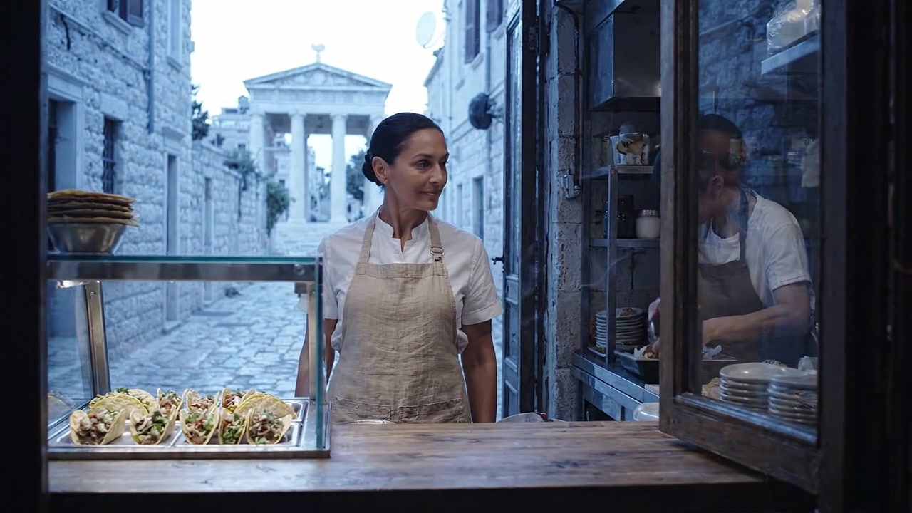 Un artista culinario fuori da un grazioso locale con vista su un'antica attrazione, che espone deliziose prelibatezze con sorrisi calorosi e un'atmosfera invitante.
