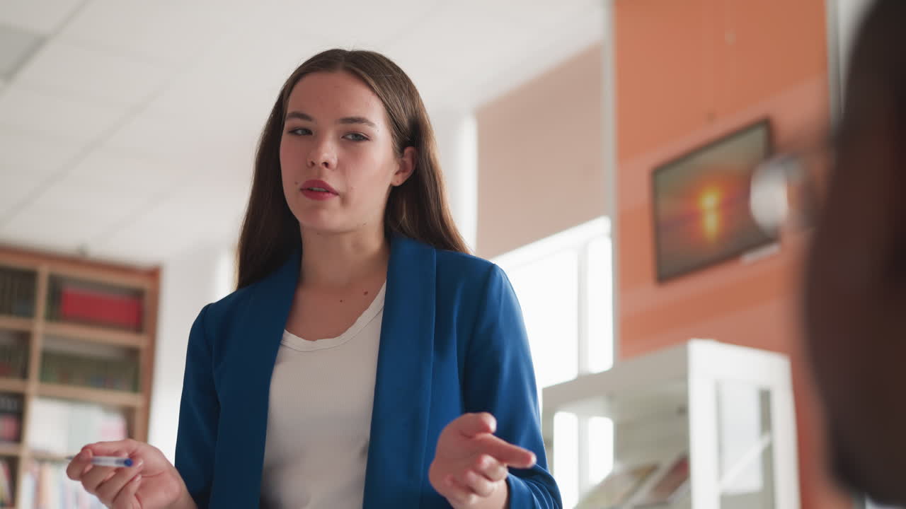 una maestra explica material a los estudiantes. una joven en uniforme de oficina le dice a los visitantes las reglas de comportamiento en la biblioteca de la universidad para evitar violaciones