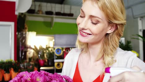 female florist spraying water on bunch of flowers in flower shop