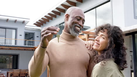 Retrato-De-Una-Feliz-Pareja-Birracial-Abrazando-Y-Sosteniendo-Llaves-En-Una-Casa-Nueva,-Cámara-Lenta