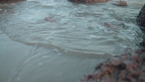 slow-motion waves retreating at rocky beach shore, tide pulling back gently with serene motion