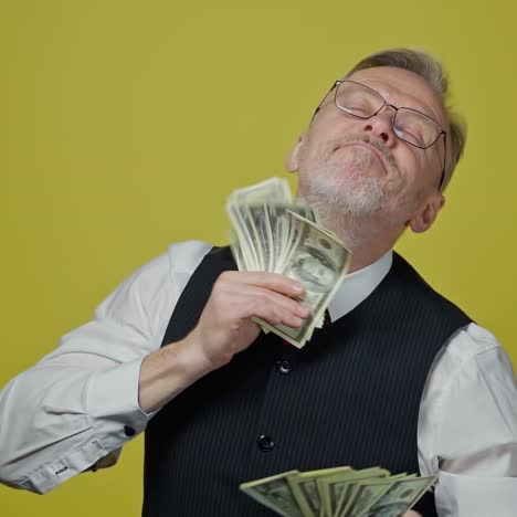 Happy elderly man with money in his hands. Dollar bills in the hands of an old cheerful man. Businessman dancing with money in yellow studio. Slow motion.
