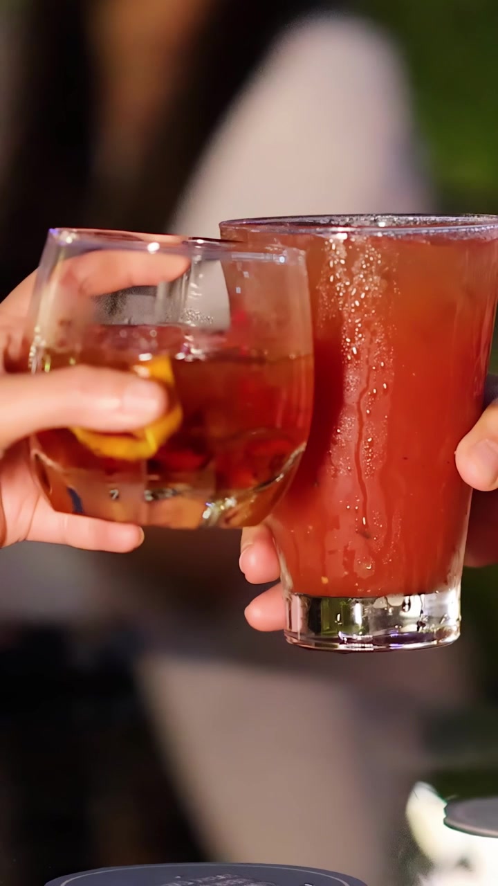 Due persone brindano con cocktail colorati in un elegante bar all'aperto, illuminazione serale calda, messa a fuoco ridotta